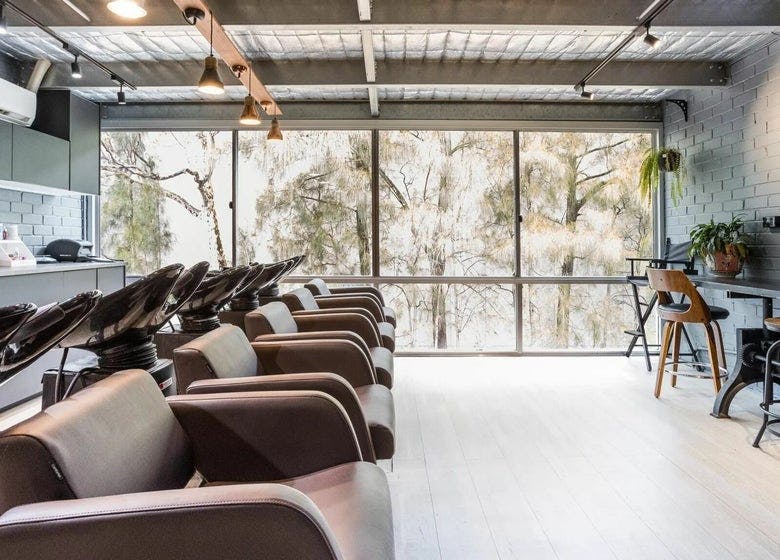 A modern hair salon with sleek black wash chairs facing floor-to-ceiling windows that look out onto trees