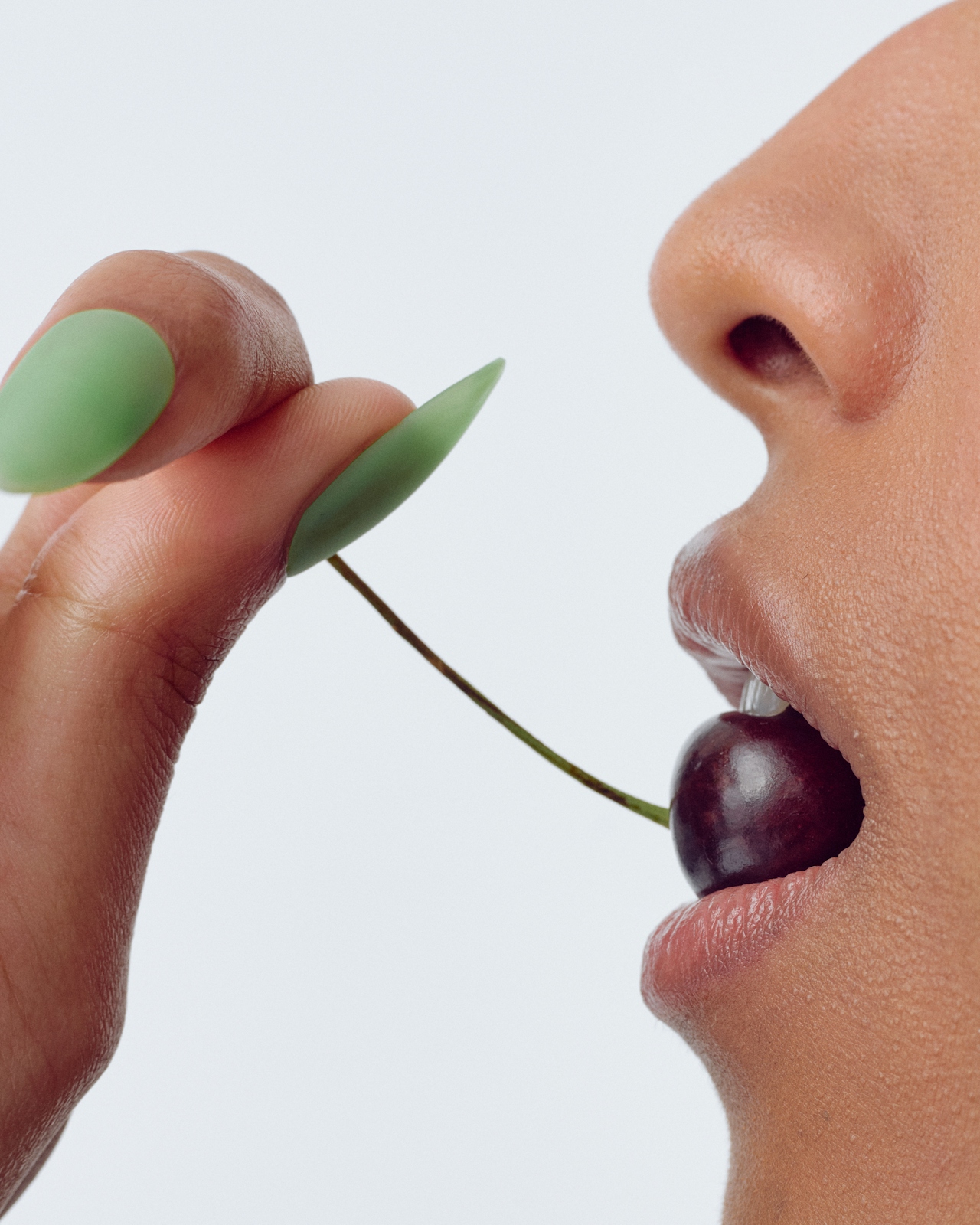 Mint-green almond nails holding a dark cherry