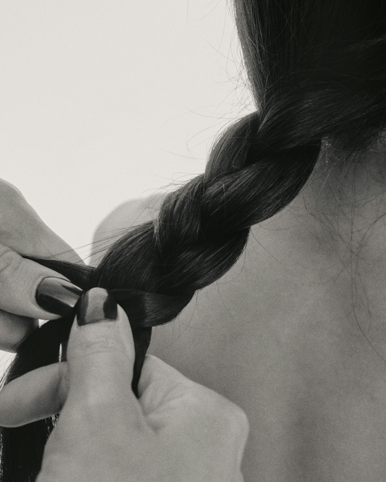 Black-and-white close-up of hands braiding long dark hair from behind